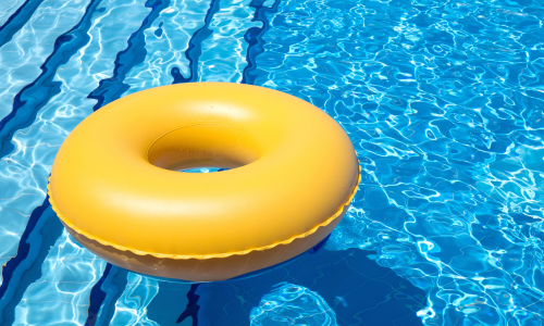 Bright yellow inflatable pool ring floating on the surface of a clear blue swimming pool with striped patterns of light reflecting on the water.